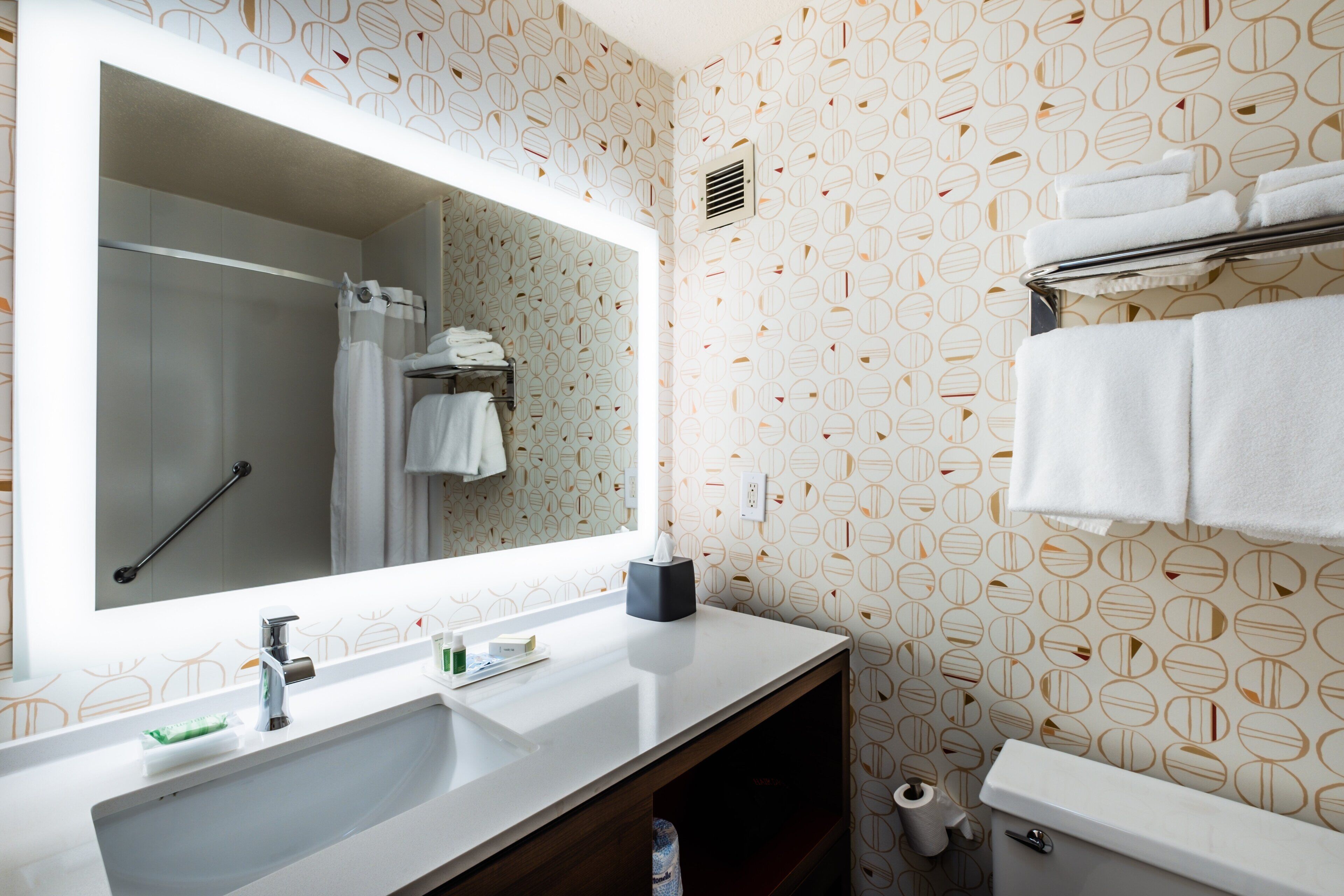 A bathroom with a large mirror, a sink, a toilet, and a towel rack.