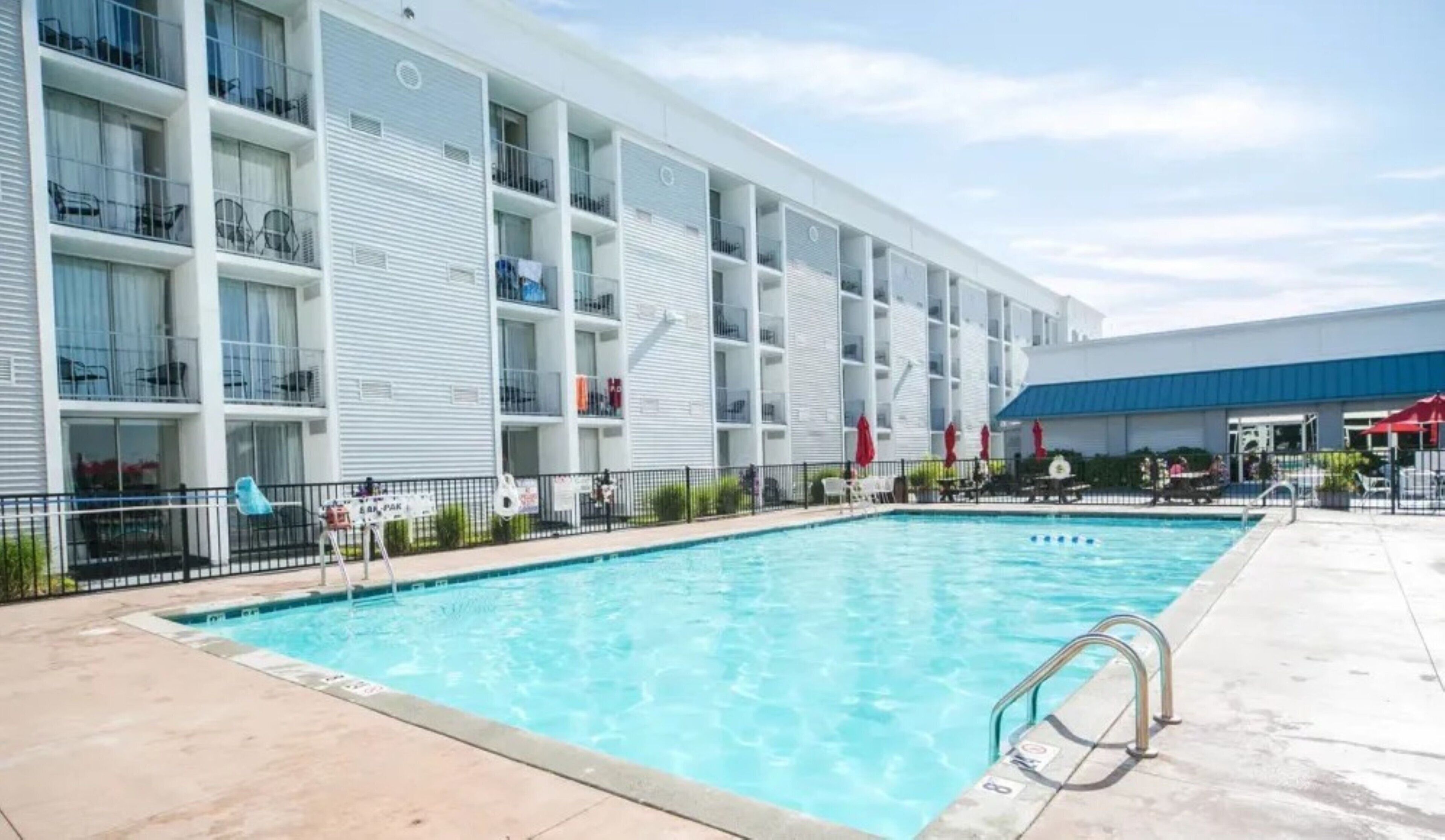 A hotel with a swimming pool, multiple balconies, and a covered area with umbrellas.