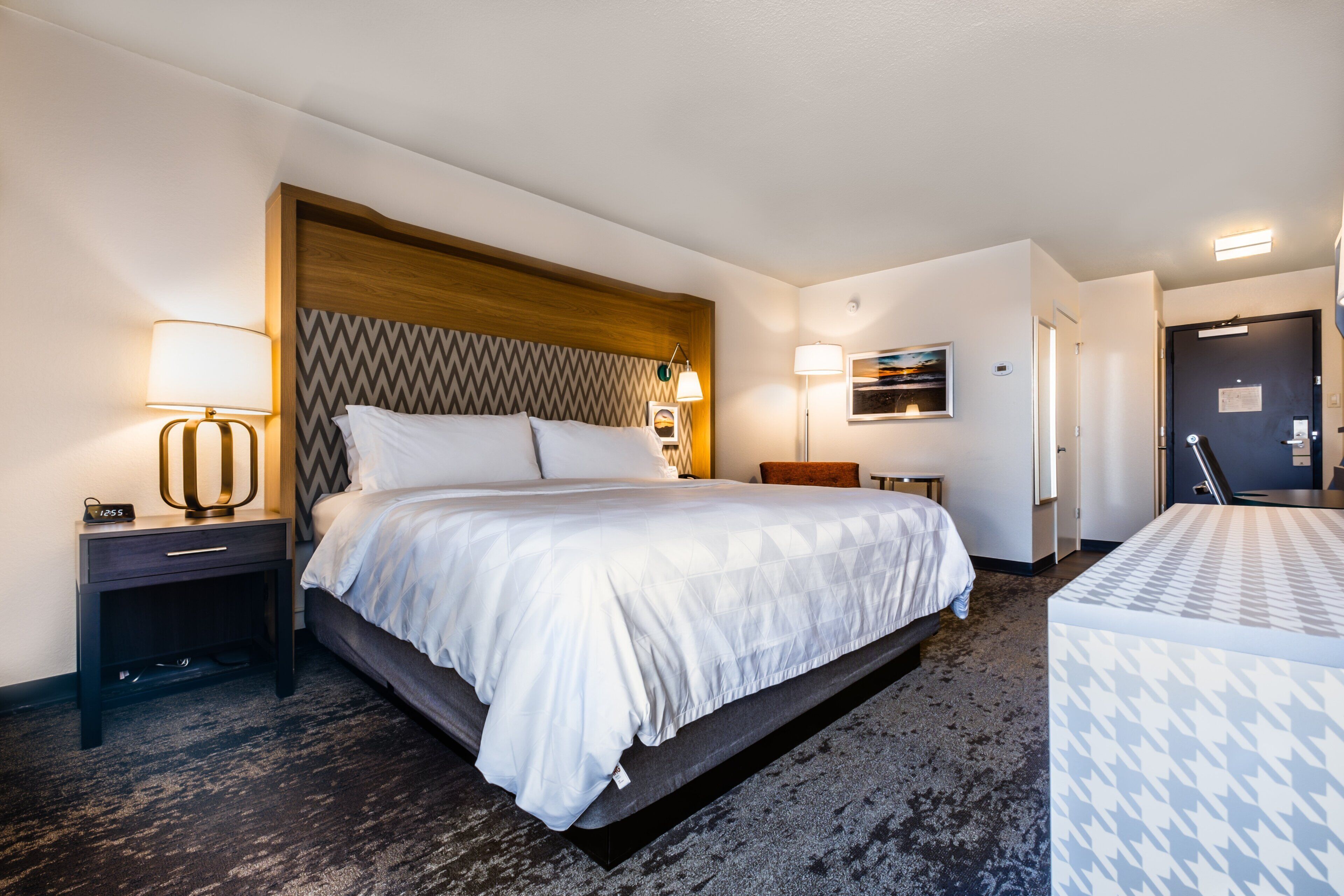 A hotel room with a bed, bedside tables, a lamp, a painting, and a door.