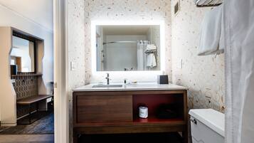 A bathroom with a vanity, a mirror, a shower, and a towel rack.