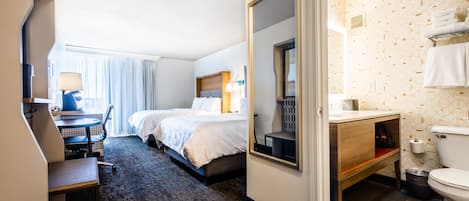 Habitación de hotel con cama, escritorio, silla, baño con inodoro y espejo.