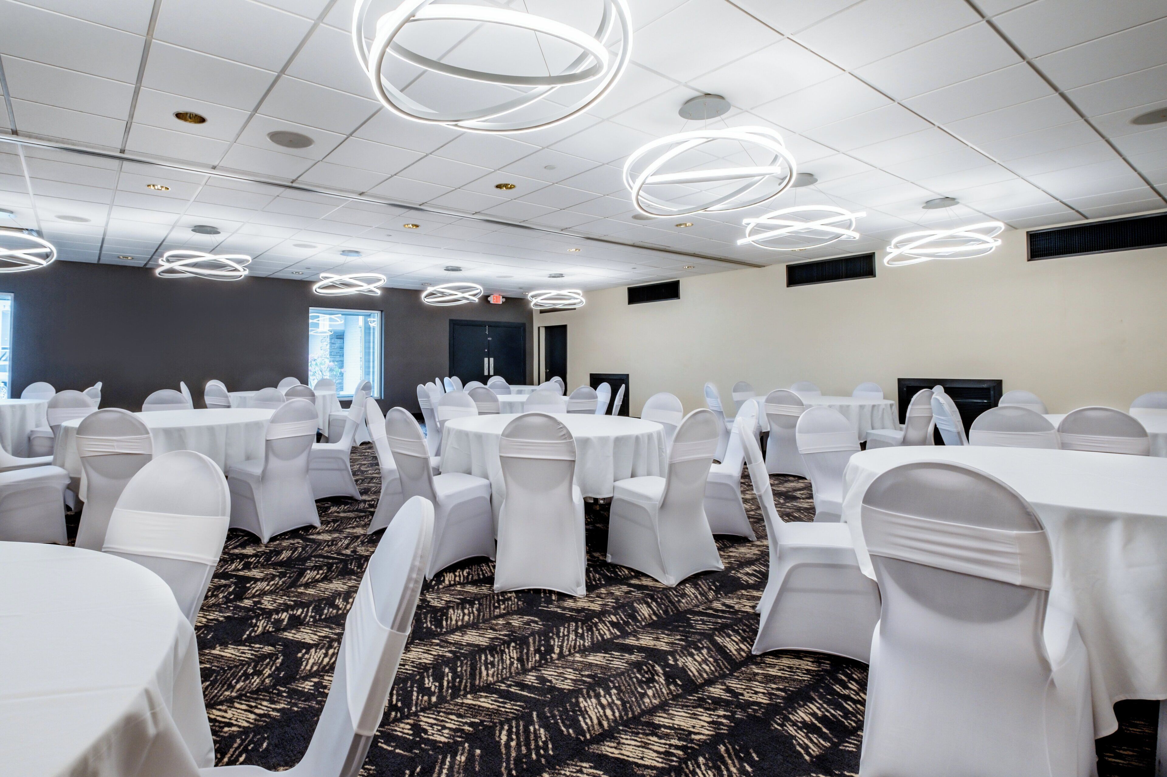 A conference room with round tables, white chairs, and modern ceiling lights.