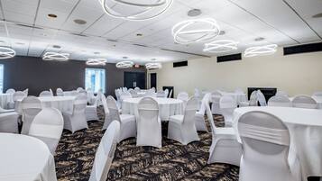 A conference room with round tables, white chairs, and modern ceiling lights.