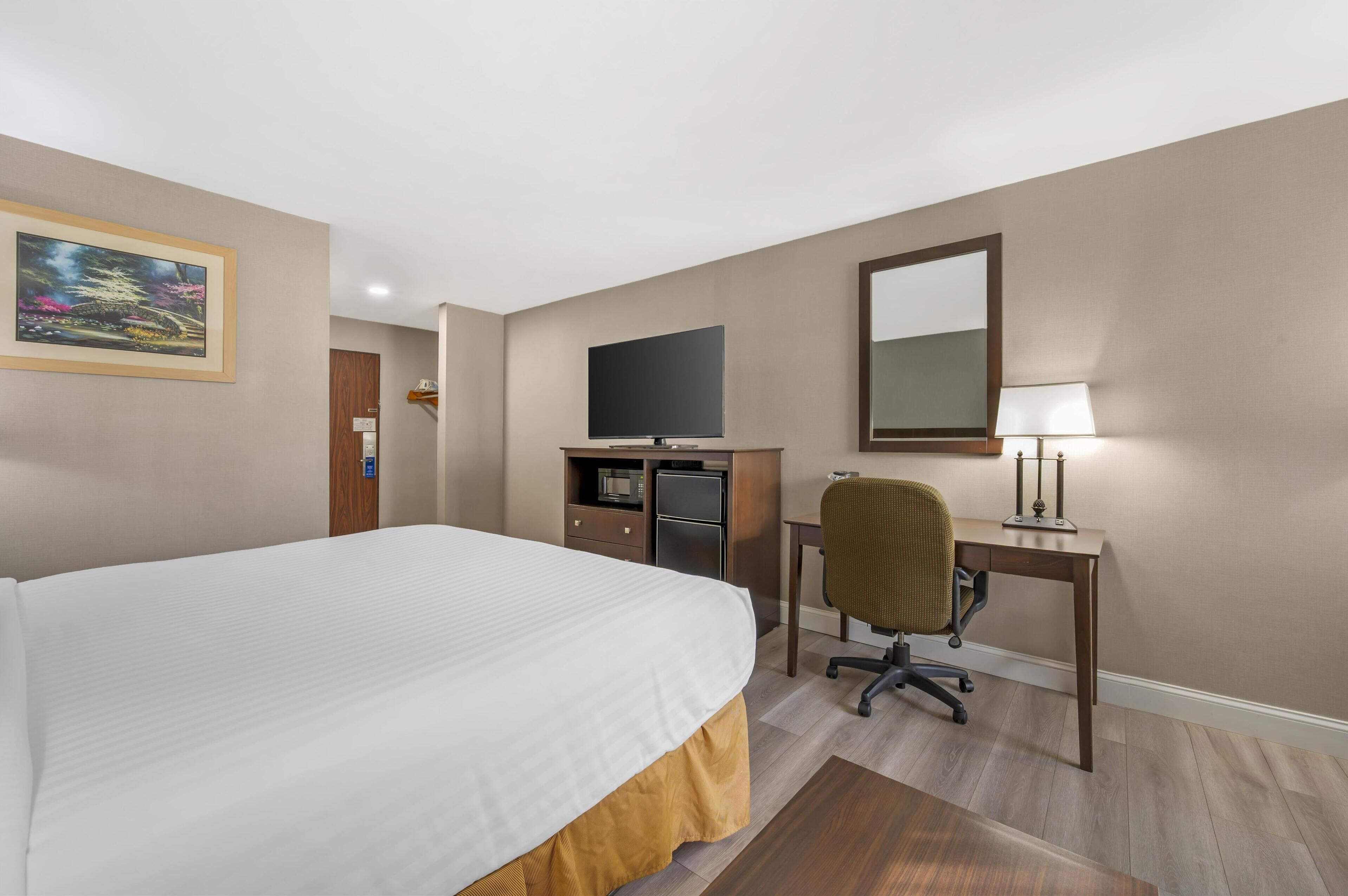 Una habitación de hotel con una cama grande, un escritorio con computadora, un televisor y un espejo.