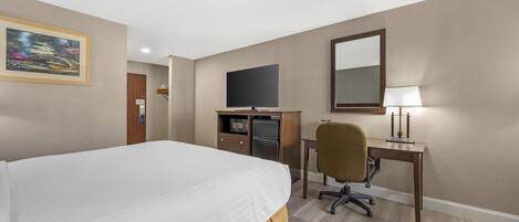 A hotel room with a large bed, a desk with a computer, a television, and a mirror.
