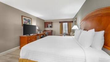 Habitación de hotel con una cama grande, un escritorio con computadora, televisor y ventana con cortinas.