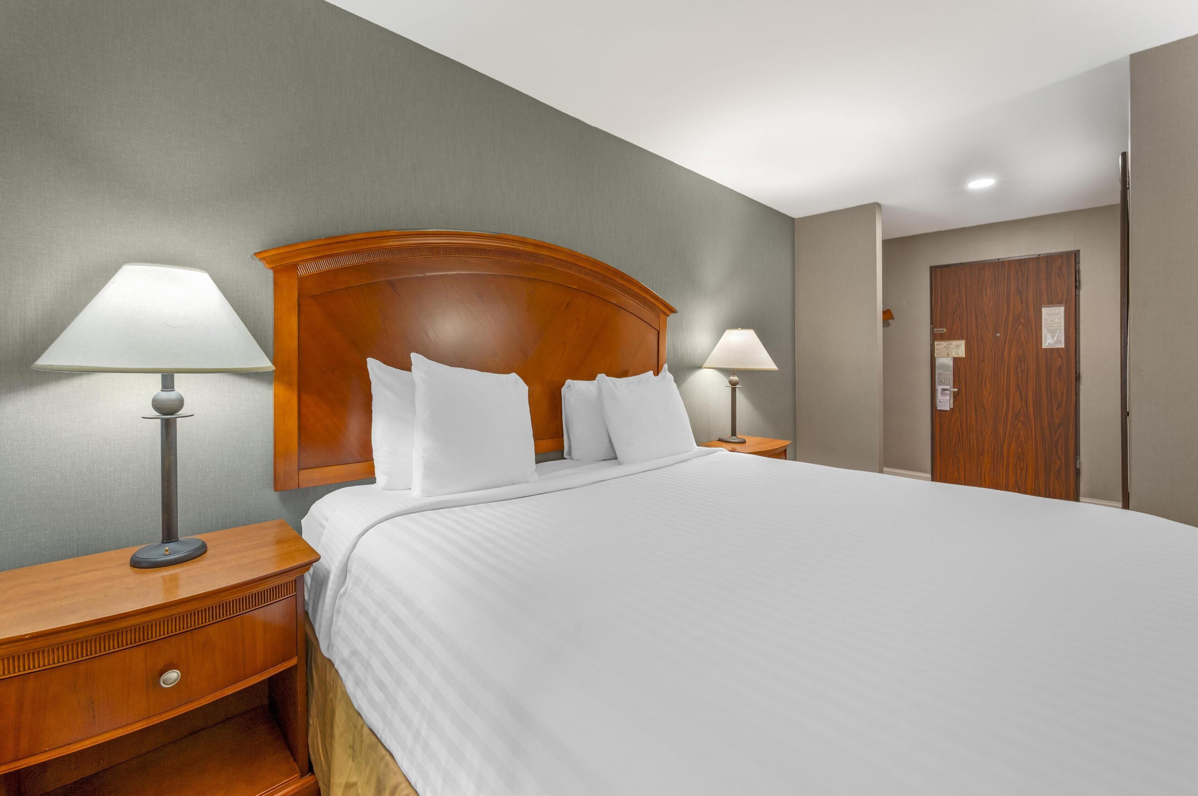 A hotel room with a large bed, two bedside lamps, a wooden headboard, and a door with a small window.