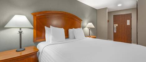 A hotel room with a large bed, two bedside lamps, a wooden headboard, and a door with a small window.