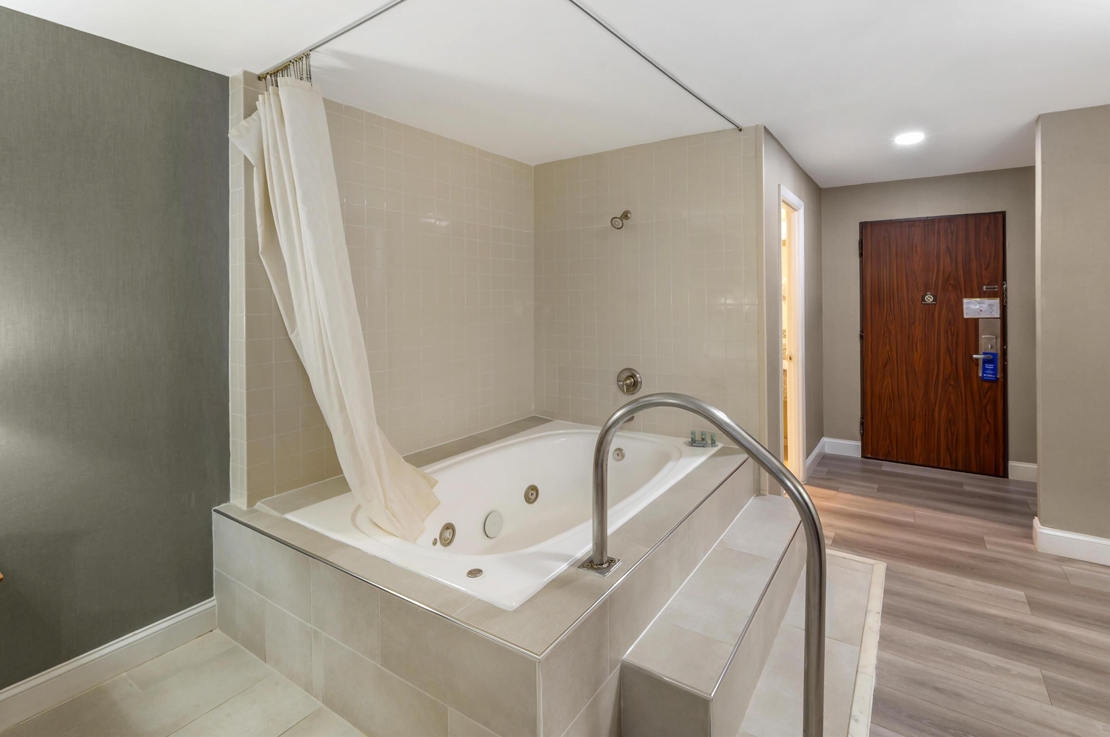 A modern bathroom with a freestanding bathtub, a shower curtain, and a wooden door.