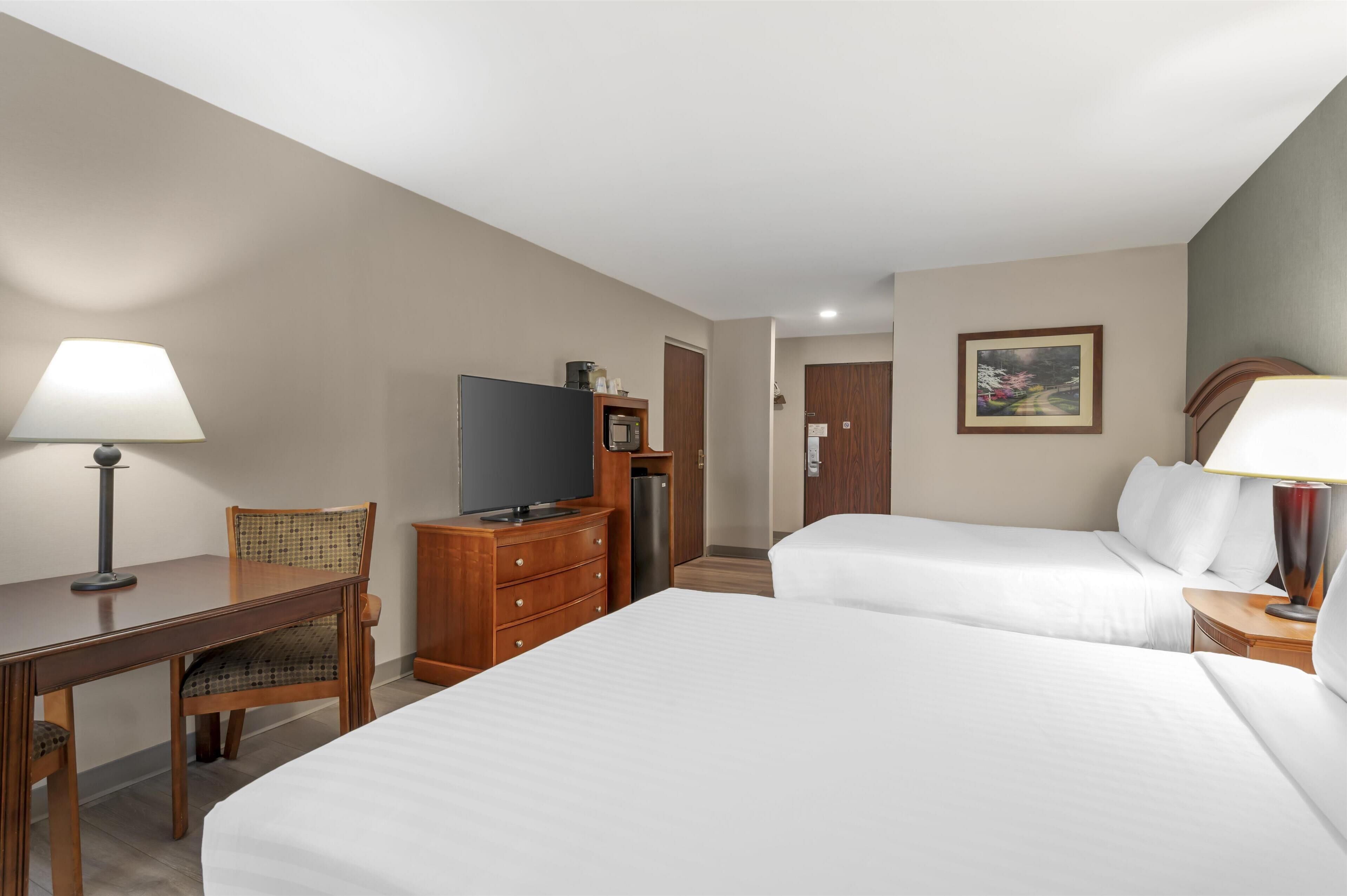 Ein Hotelzimmer mit zwei Betten, einem Schreibtisch, einem Fernseher und einem Kühlschrank.