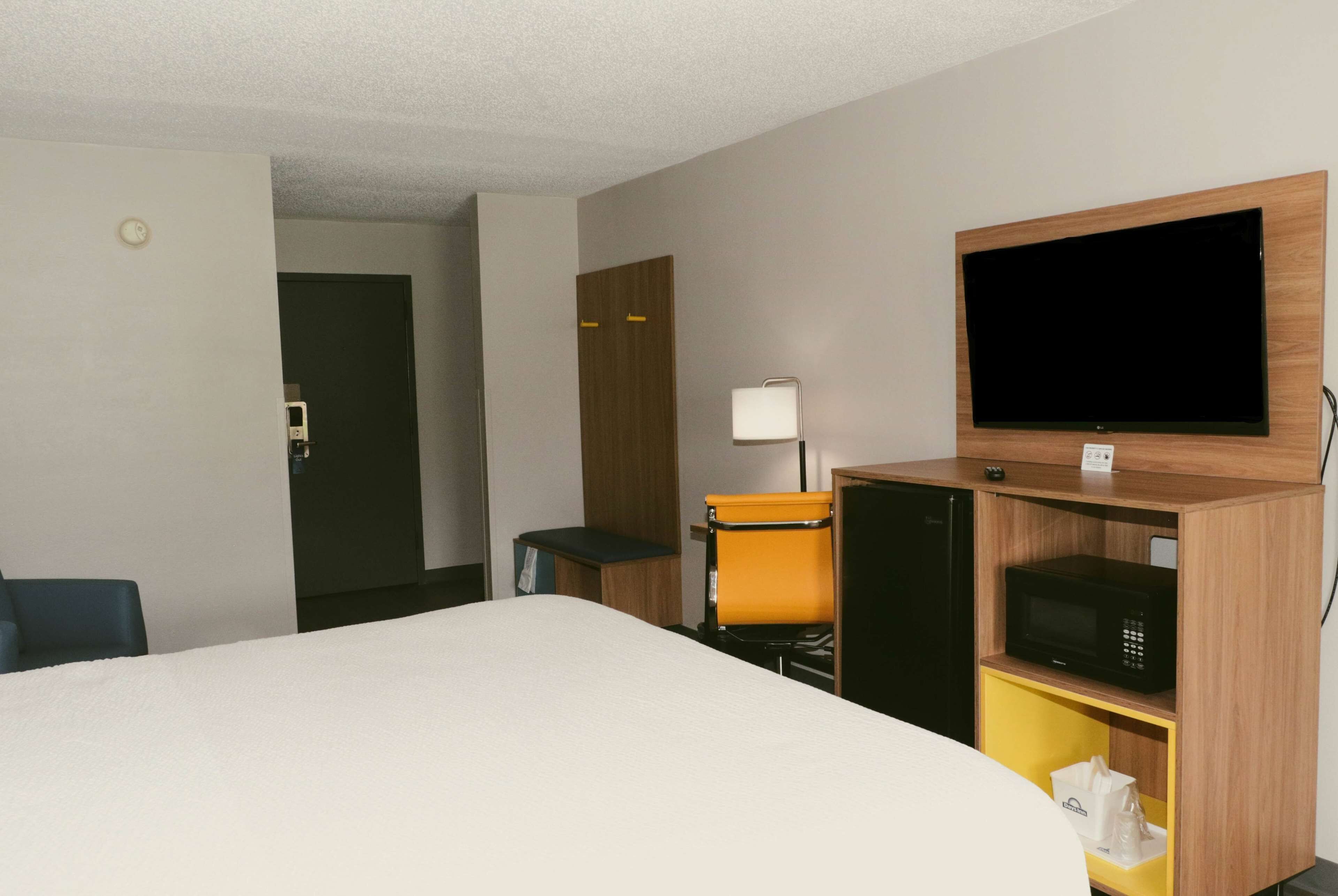 Quarto de hotel com cama, televisão na parede, micro-ondas, mesa pequena e uma cadeira.
