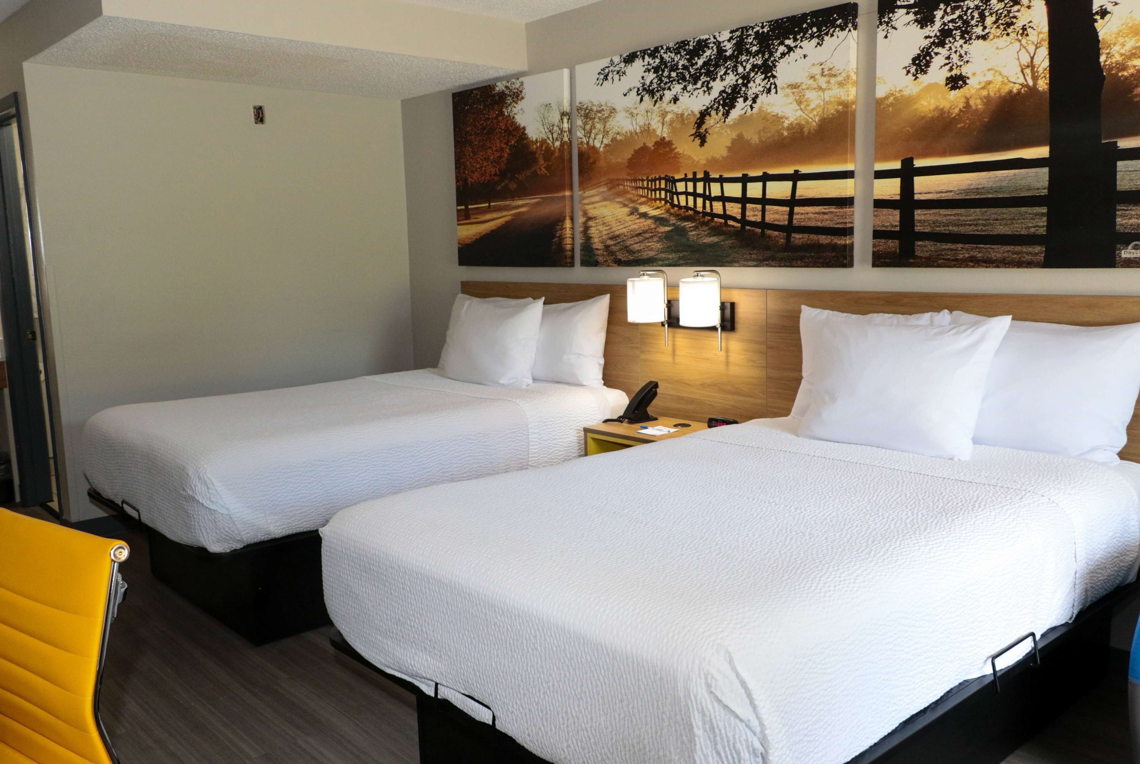 Ein Hotelzimmer mit zwei Betten, einem Holzkopfende, einem Nachttisch mit Lampe und einem Wandbild mit Sonnenuntergang.