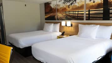 A hotel room with two beds, a wooden headboard, a nightstand with a lamp, and a painting of a sunset scene on the wall.
