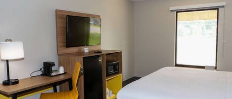 Una habitación de hotel con una cama, un escritorio con una silla, un televisor, un microondas y un refrigerador pequeño.