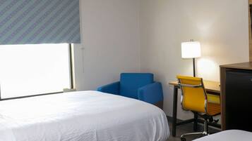 A hotel room with a bed, a desk with a chair, and a lamp.