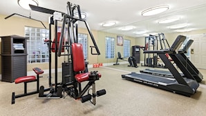 Un gimnasio con equipo de ejercicio, una cinta de correr y un espejo que refleja la sala.