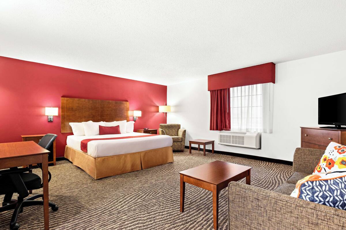 A hotel room with a bed, a desk, a chair, a sofa, a TV, and a window with curtains.