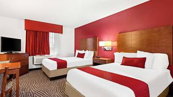 Habitación de hotel con dos camas, un escritorio, un televisor y una ventana con cortinas rojas.