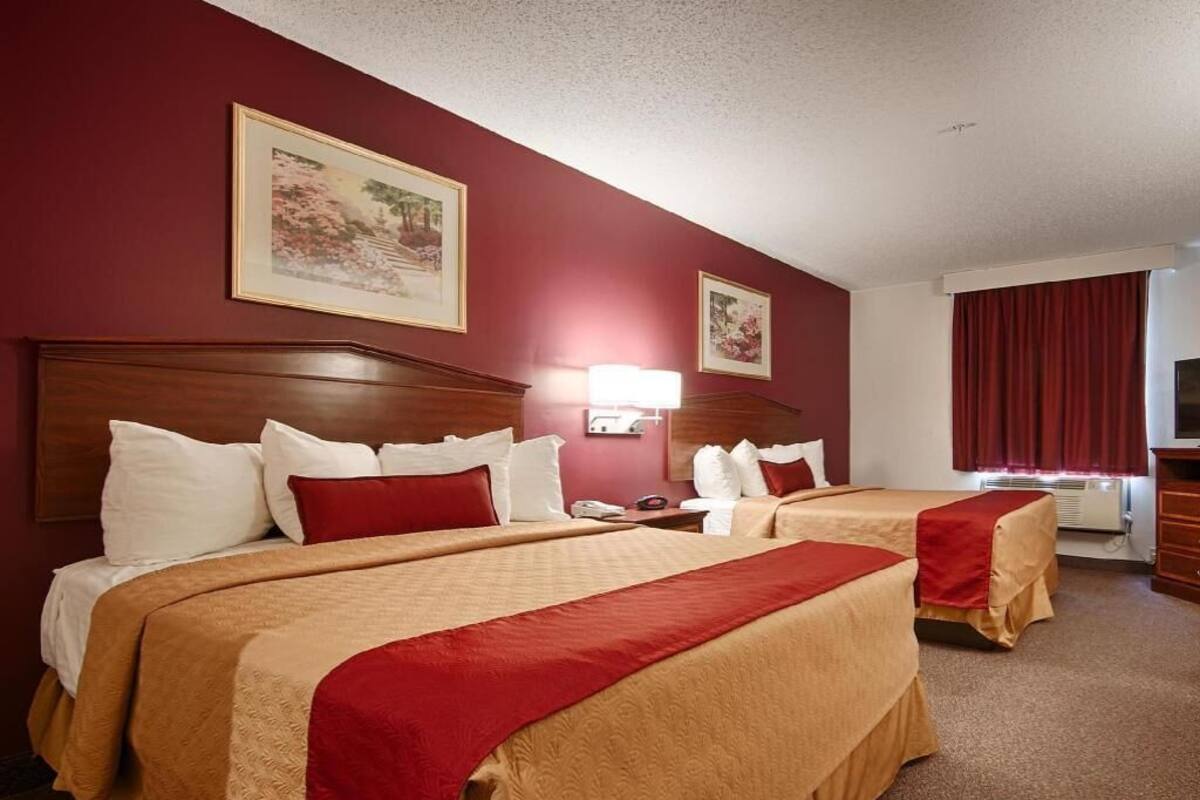 A hotel room with two beds, a wooden headboard, a red curtain, and a painting on the wall.