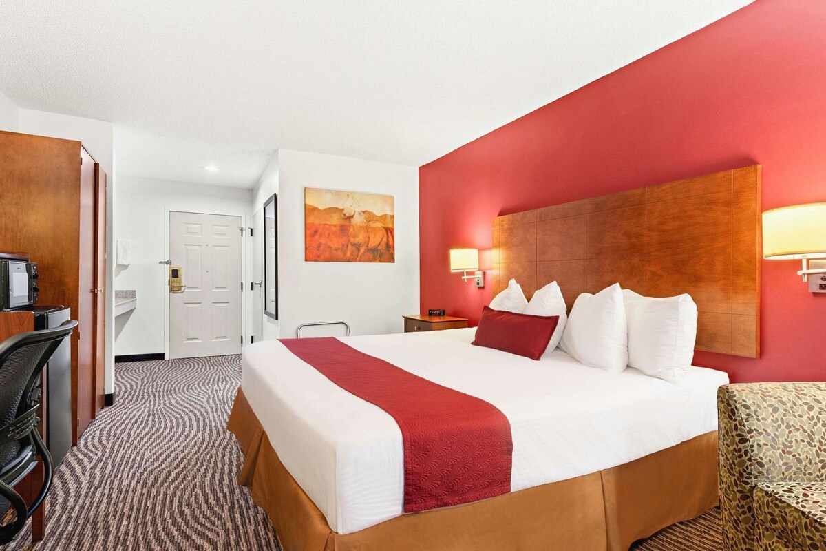 A hotel room with a large bed, a desk, a chair, a desk lamp, and a painting on the wall.
