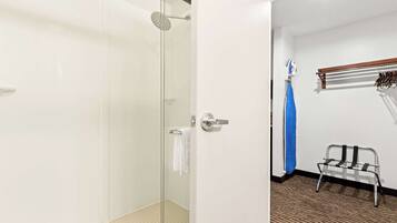 A hotel bathroom with a glass shower enclosure, a towel rack, and a bench.