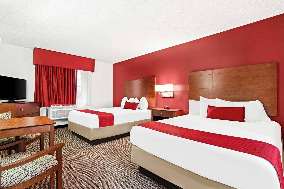 A hotel room with two beds, a TV, a desk, and a chair.