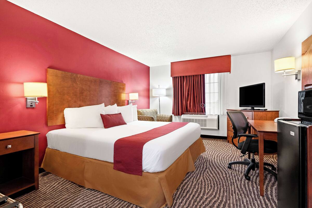A hotel room with a large bed, a desk with a computer, a television, and a minibar.