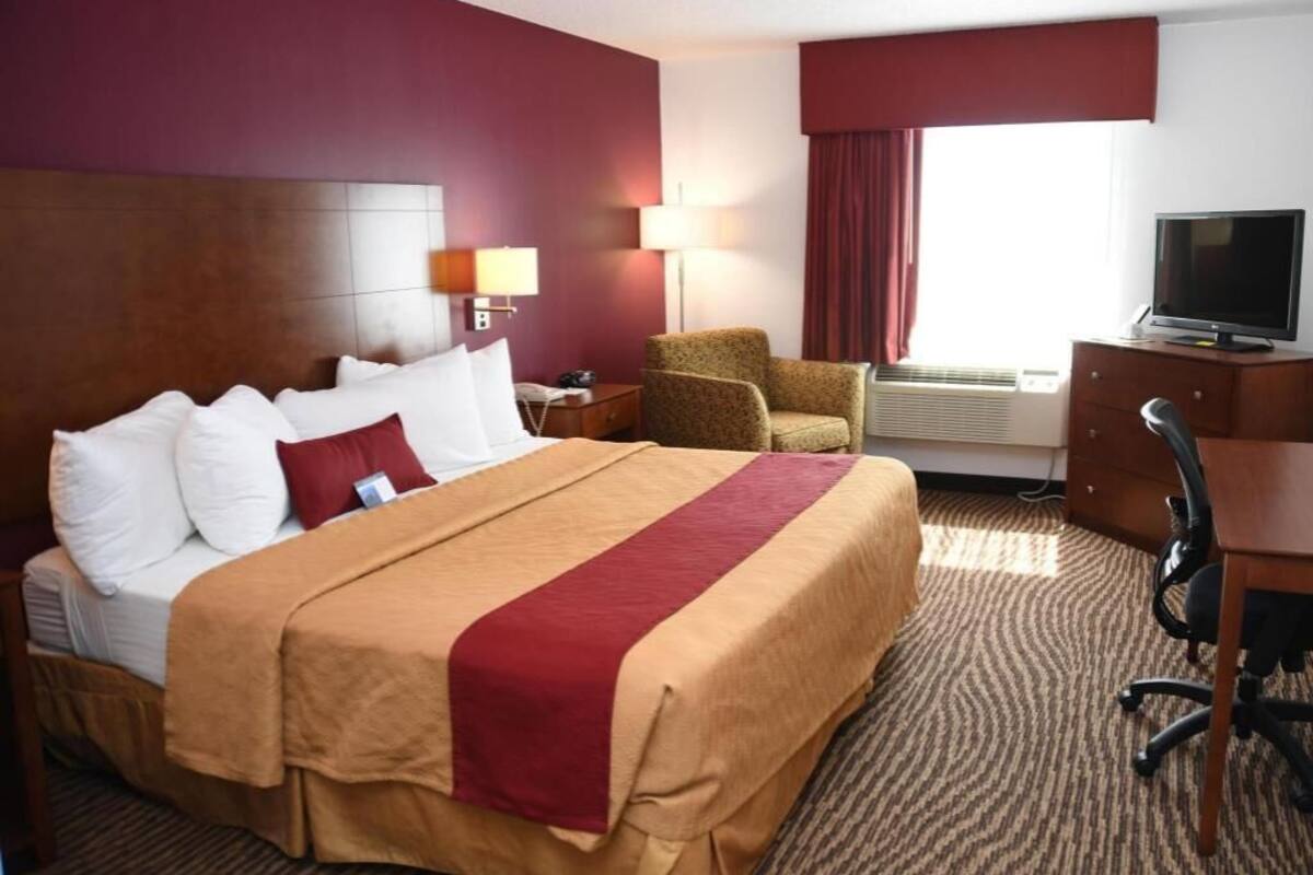 A hotel room with a large bed, a desk, a chair, a television, and an air conditioning unit.
