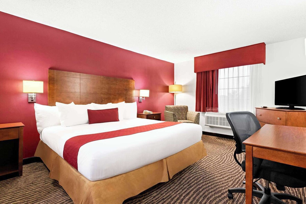 Habitación de hotel con una cama grande, un escritorio, una silla, un televisor y una ventana con cortinas.