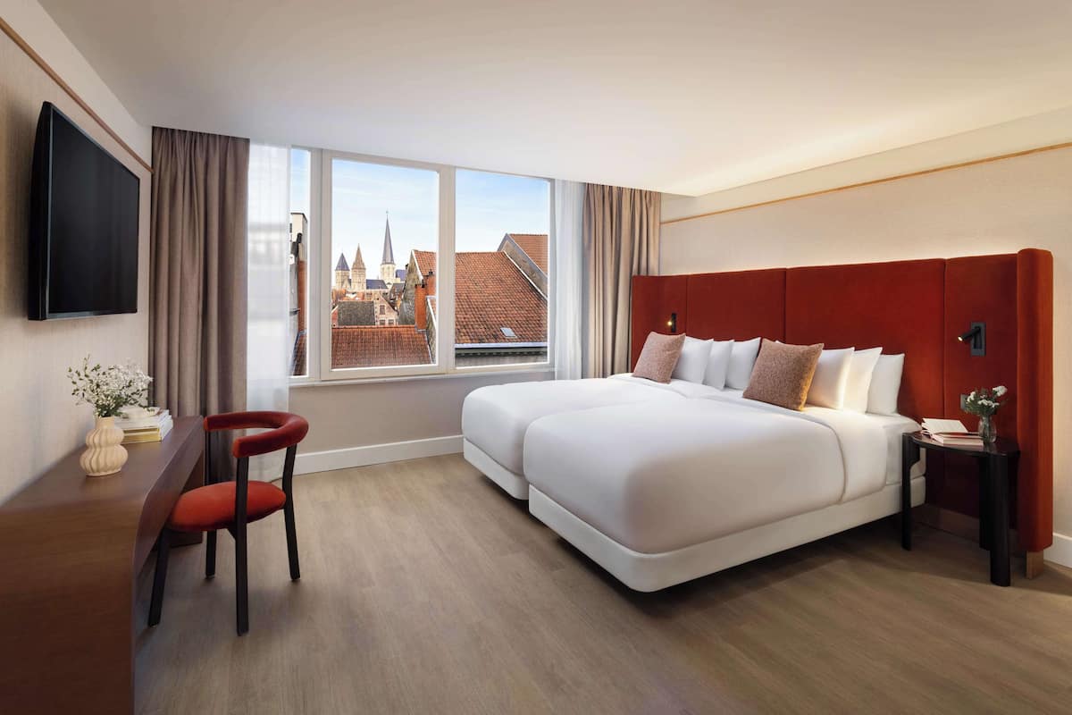 Habitación de hotel con una cama grande, un escritorio, una silla, un televisor y una ventana con vistas a la ciudad.
