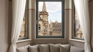 Une pièce avec vue sur un bâtiment historique, visible à travers une fenêtre ornée de rideaux.