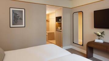 A hotel room with a bed, a bedside table with a vase, a large mirror, and a wardrobe with a hanging rack.