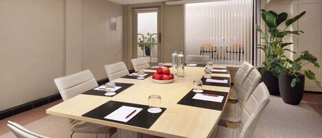A conference room with a long table, white chairs, and potted plants.