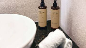 Deux flacons de savon liquide et de lotion pour le corps de la marque NATHAL, posés sur le comptoir d’une salle de bain.