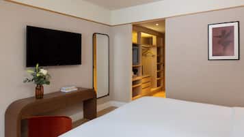 Een hotelkamer met een bed, een bureau met een bloevas, een televisie, een kledingkast en een lijst aan de muur.