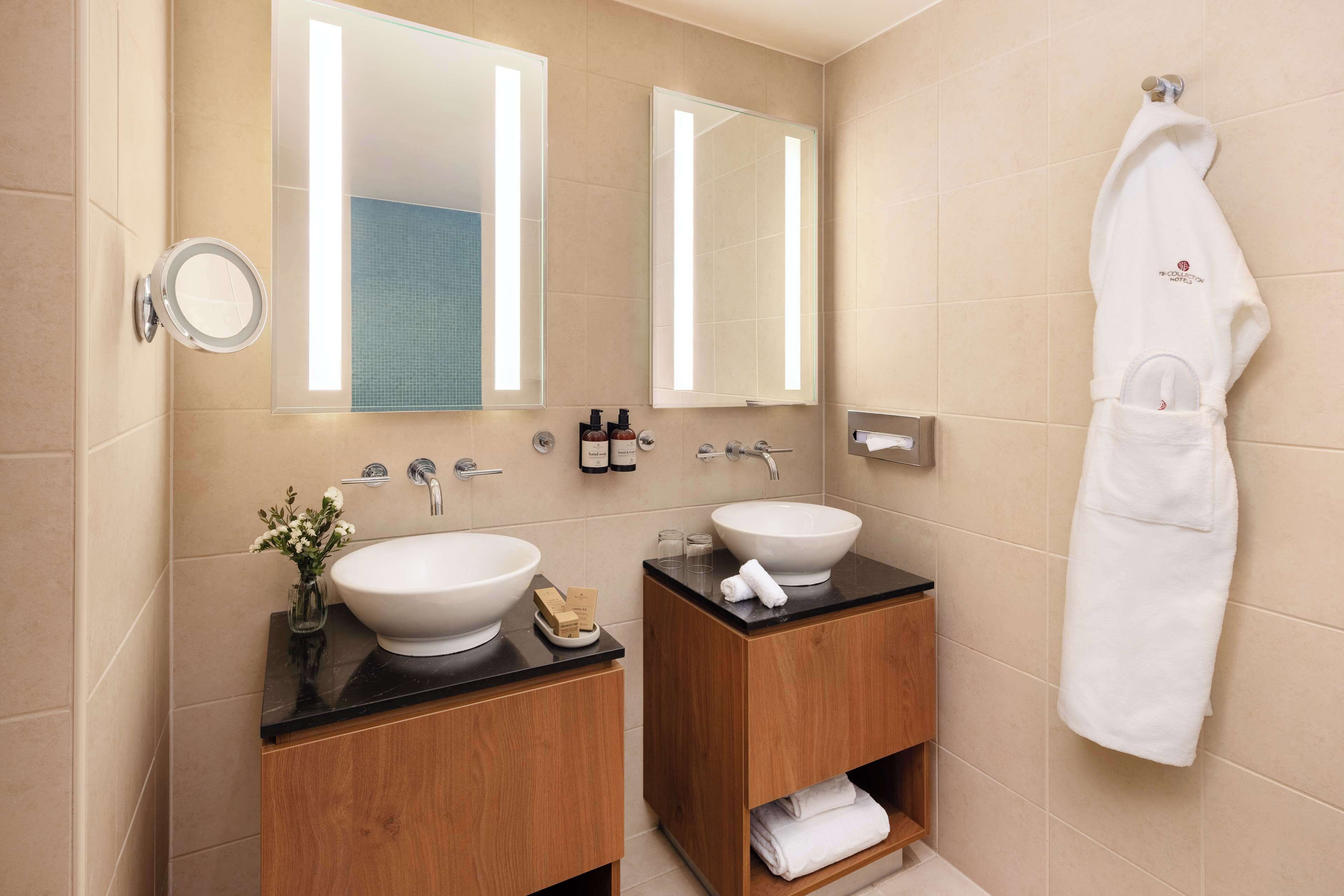 A modern bathroom with two sinks, wooden cabinets, a towel rack, and a mirror.