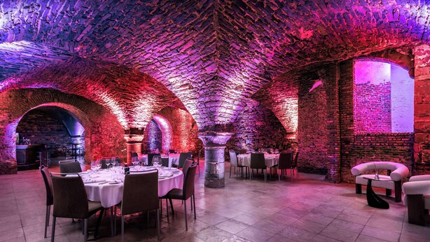Un restaurant avec des arches en briques et un sol carrelé, doté de tables et de chaises rondes.