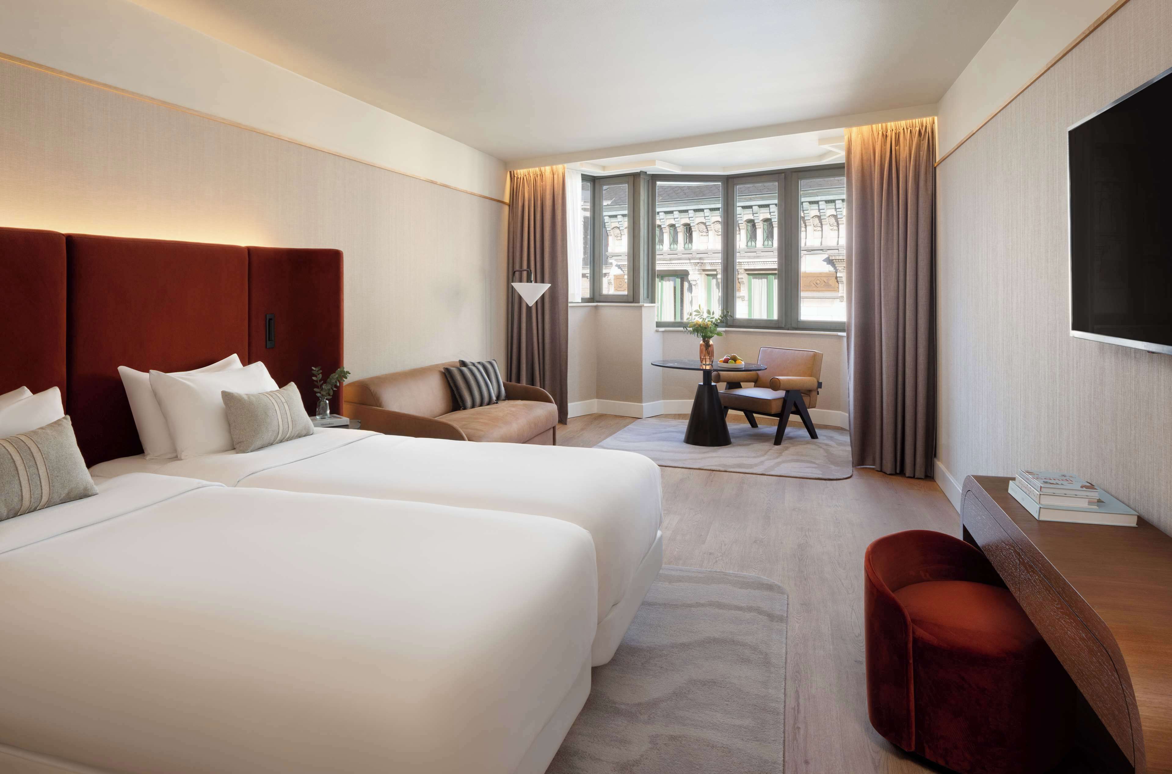 A hotel room with two large beds, a desk, a chair, and a TV.