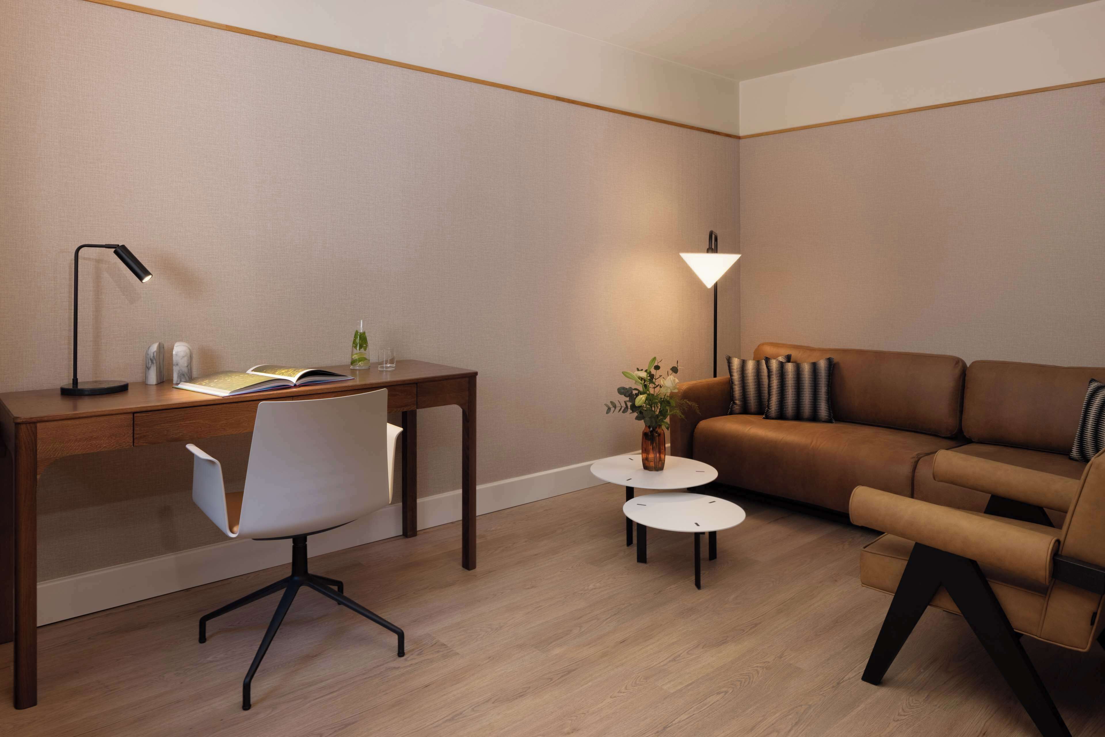 Una sala de estar moderna con un escritorio de madera, una silla blanca, un sofá marrón y una pequeña mesa redonda con un florero.