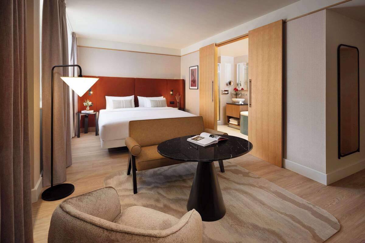 Una habitación de hotel con una cama, un sofá, una mesita, una lámpara y un espejo.
