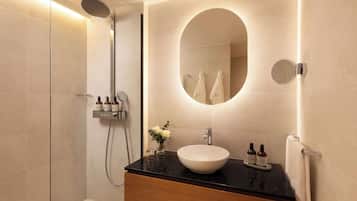 A modern bathroom with a large oval mirror, a round sink, and a shower area.