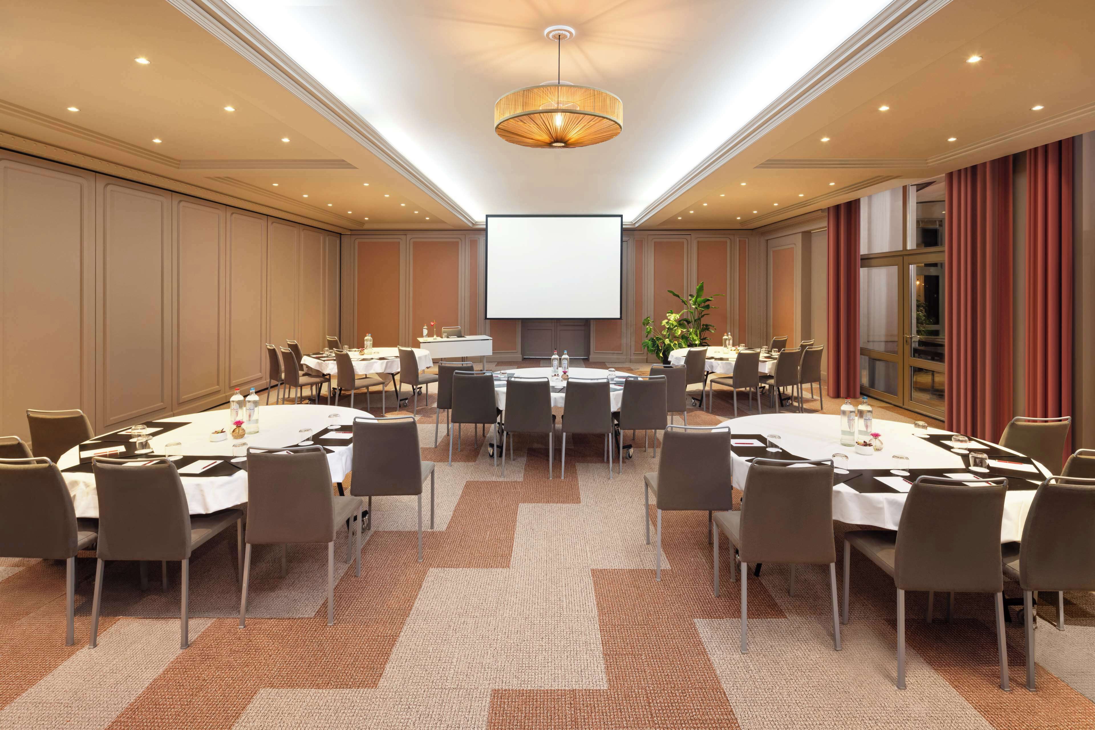 A conference room with a large screen, multiple tables, and chairs arranged for meetings.