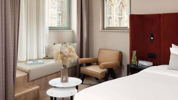 A hotel room with a large bed, a sofa, a chair, a small round table, and a window with curtains.