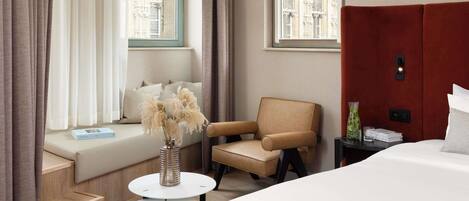 A hotel room with a large bed, a sofa, a chair, a small round table, and a window with curtains.