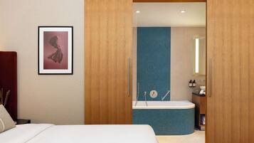 Una habitación de hotel con cama, un cuadro enmarcado en la pared, un armario de madera y un baño con bañera y lavamanos.