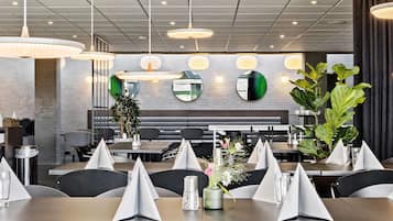 A modern restaurant interior with multiple tables, black chairs, and hanging pendant lights.