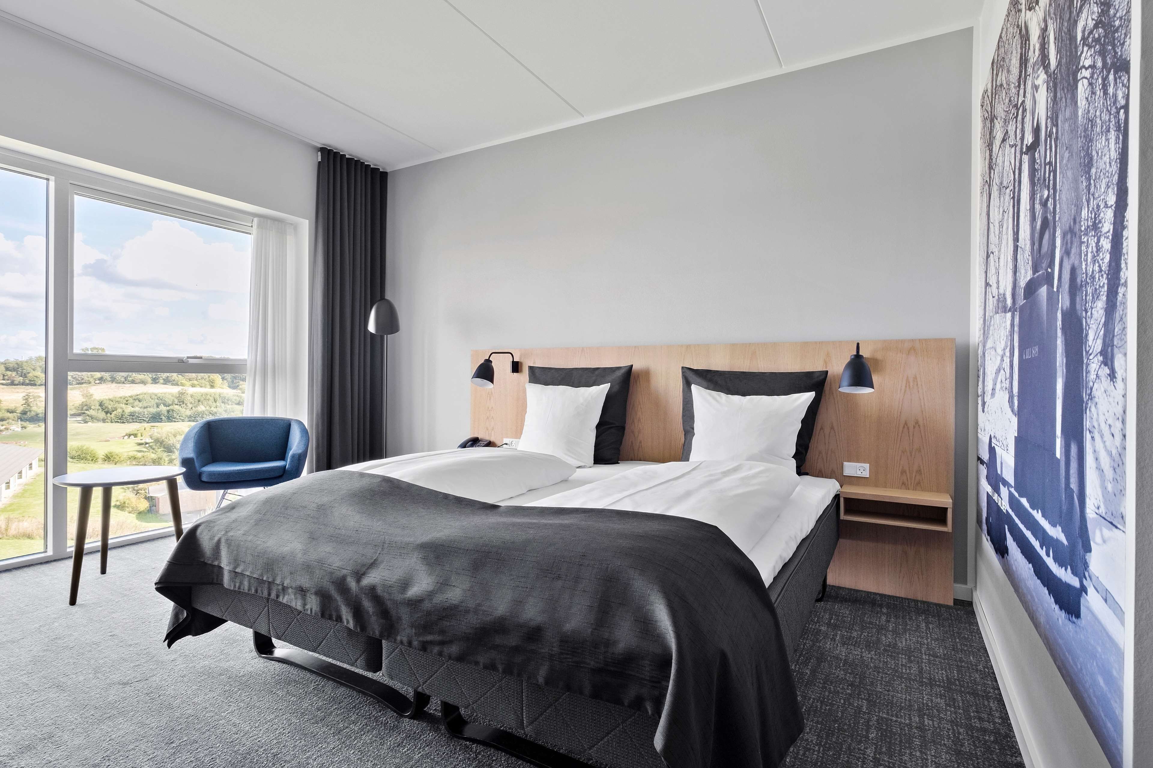 Una habitación de hotel moderna con una cama grande, una mesita de noche, una silla y vistas al exterior.