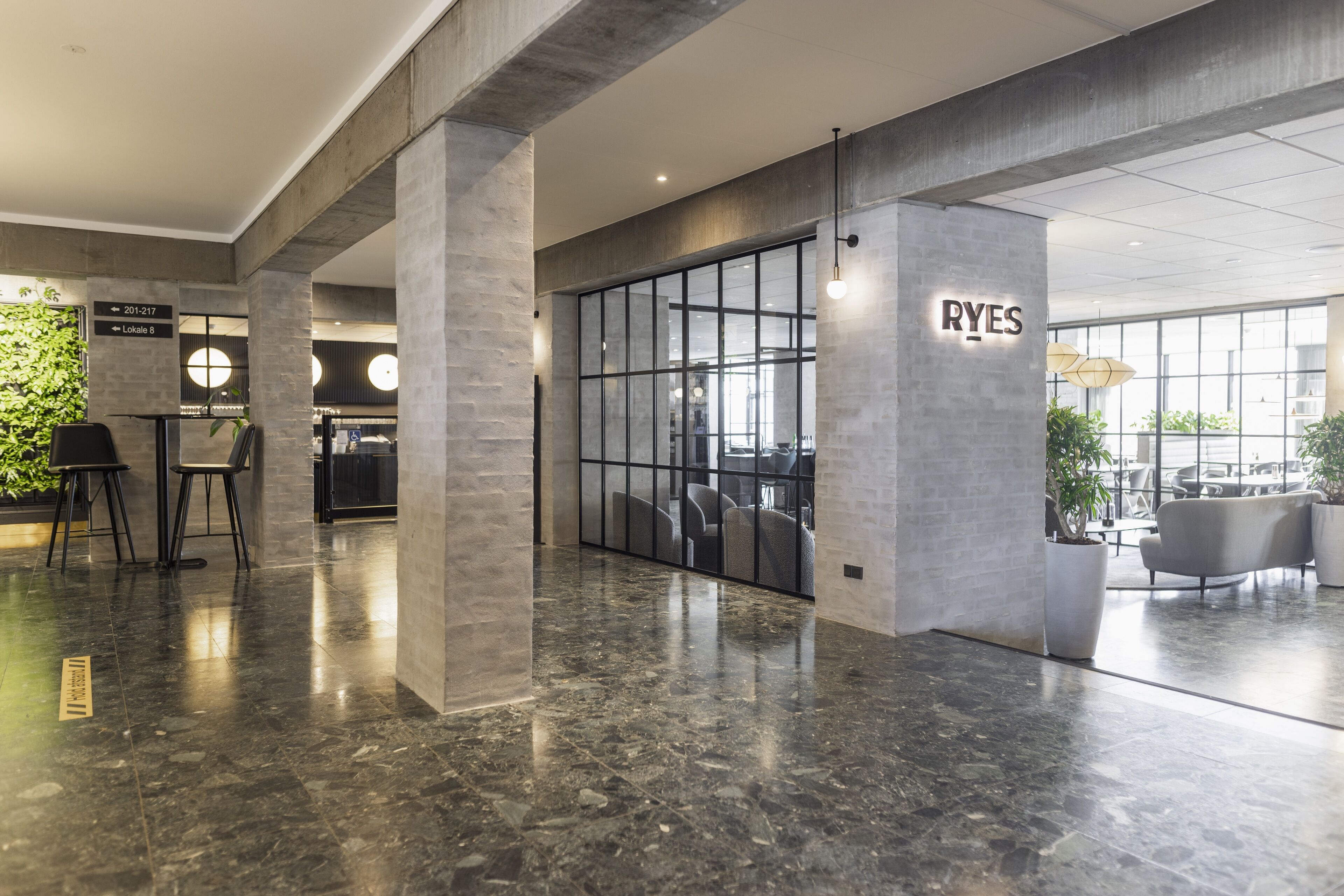 Un vestíbul modern amb sòl de marbre, zona de seients i una separació de vidre amb el cartell 'RYES'.
