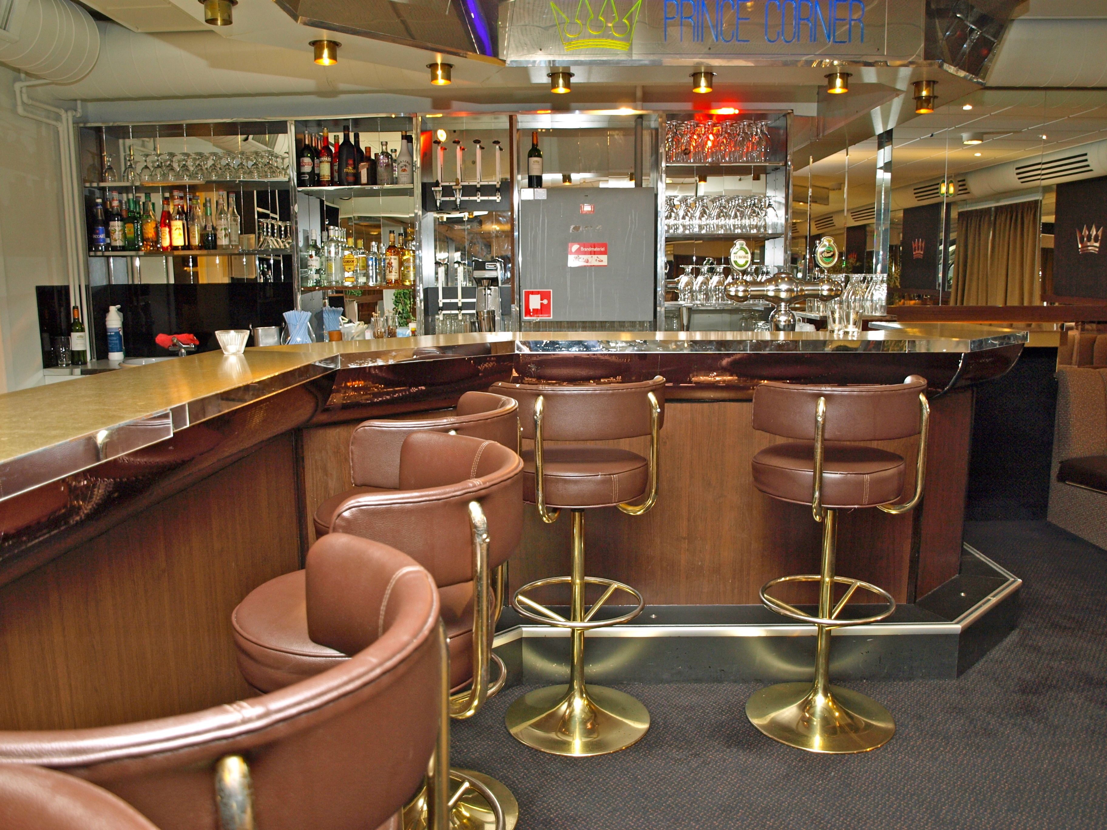 A bar area with a counter, stools, and shelves of bottles and glasses.