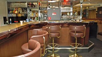 Un espace bar avec un comptoir, des tabourets et des étagères remplies de bouteilles et de verres.